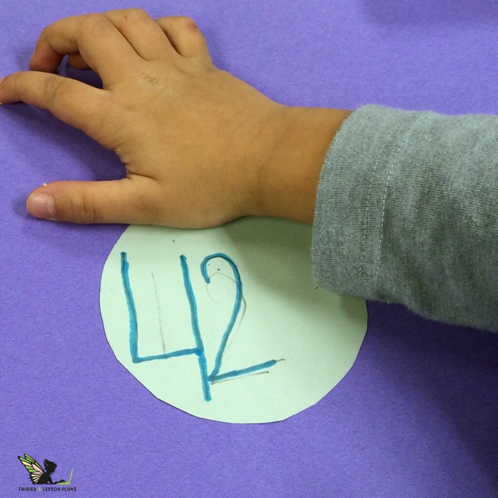 Picture of a child glueing a circle with the number forty-two onto a large piece of construction paper.